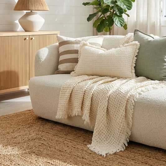 Cozy living room with a beige sofa, textured throw blanket, and decorative pillows.