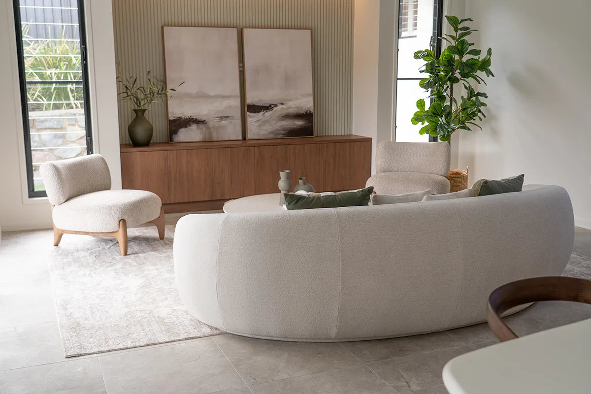 Modern living room with a white curved linen sofa, armchair, and decorative elements.