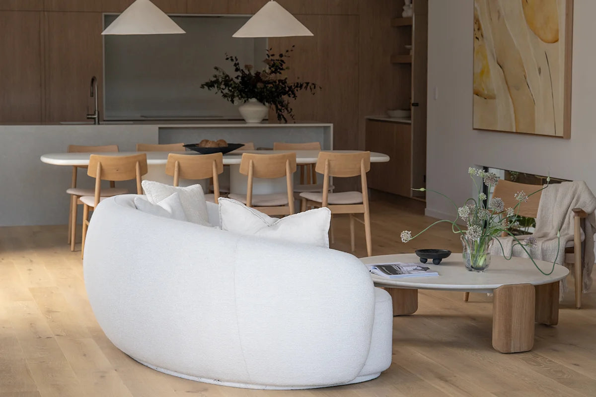 Modern living room with a white sofa, wooden chairs, and a coffee table with flowers.