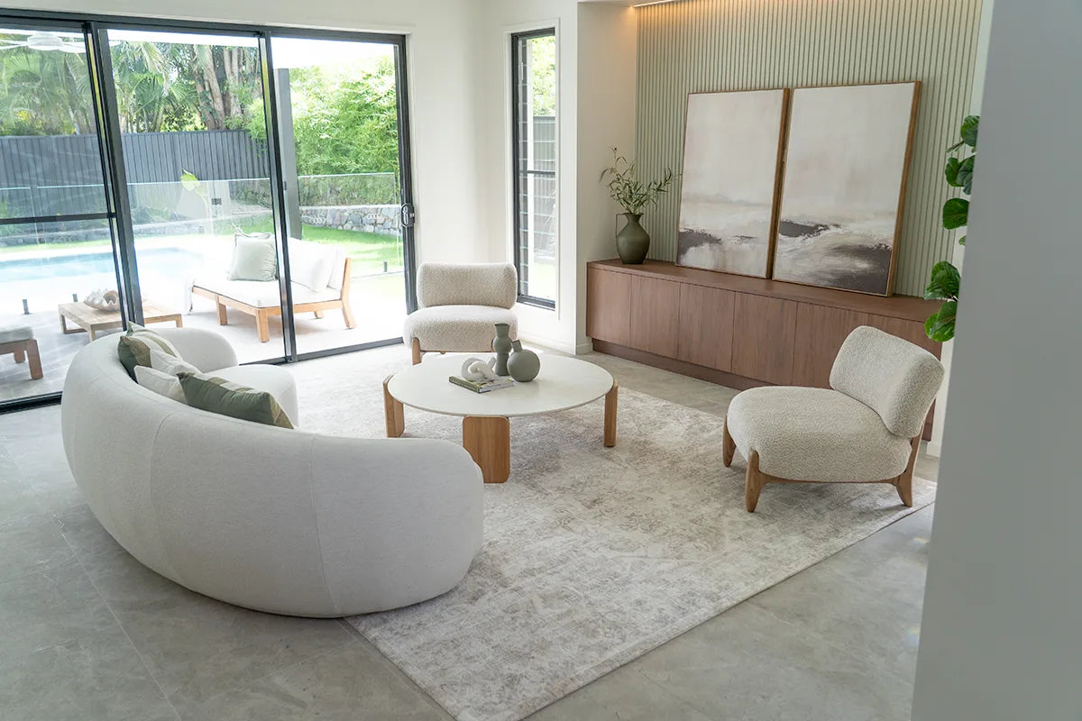 Modern living room with a curved white sofa, round coffee table, and large windows.