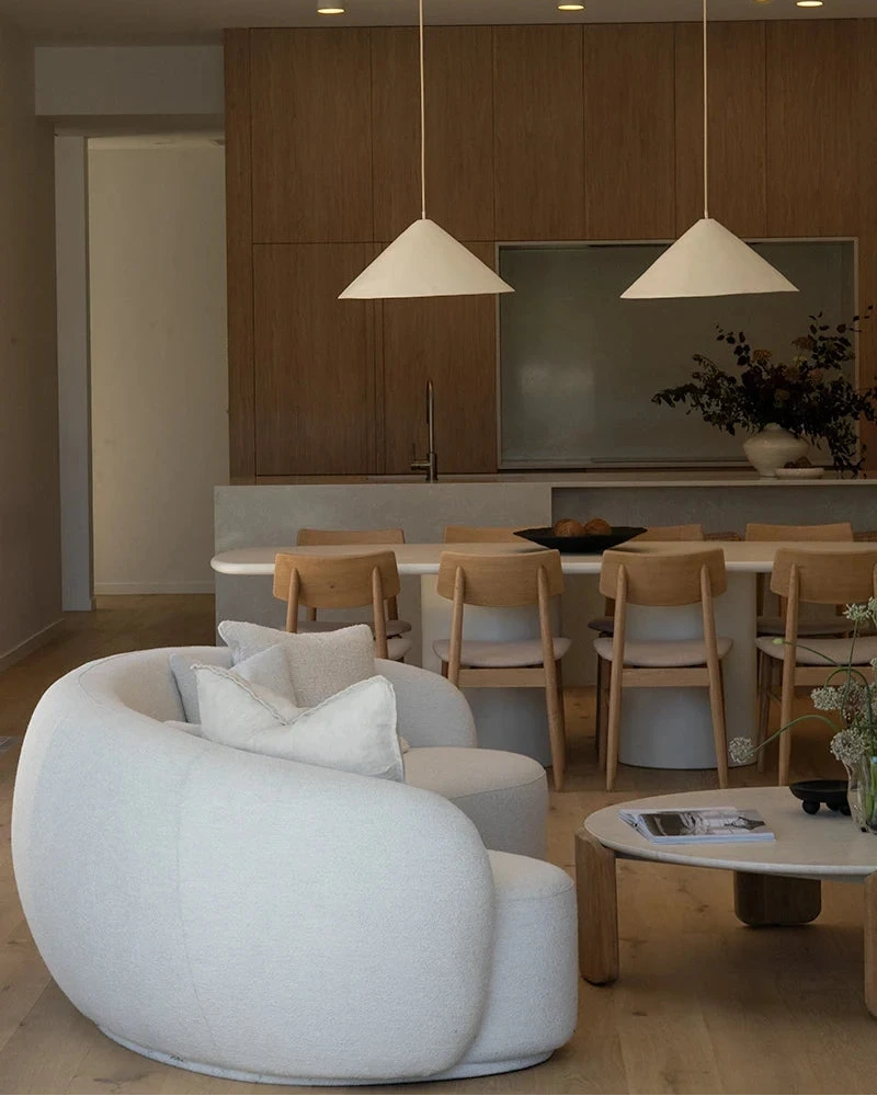 Modern living room with a white linen curved  sofa, wooden dining table, and pendant lights