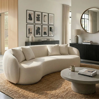 Modern living room with a curved beige sofa, round coffee table, and abstract art on the wall.