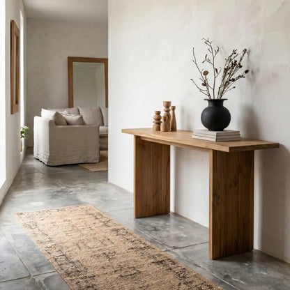 Modern interior with a wooden console table, vase with dried plants, and sofa in a well-lit room.