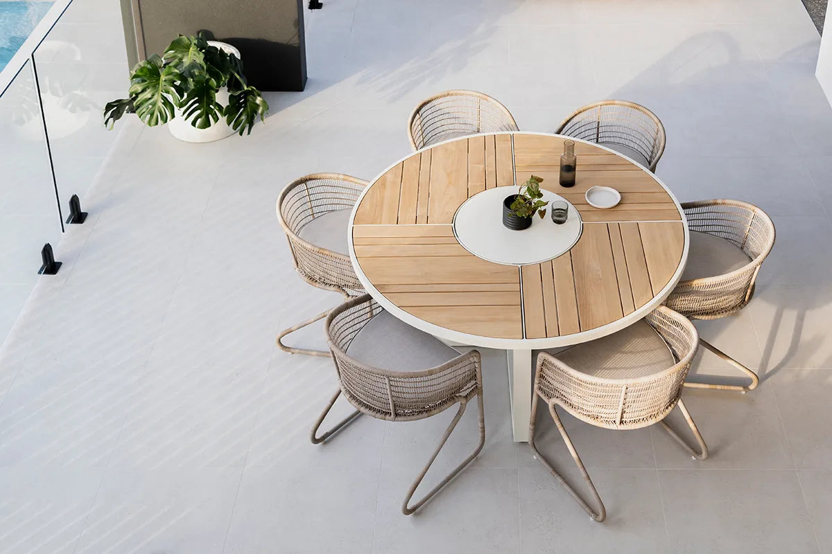 Round wooden table with six wicker chairs on a white patio
