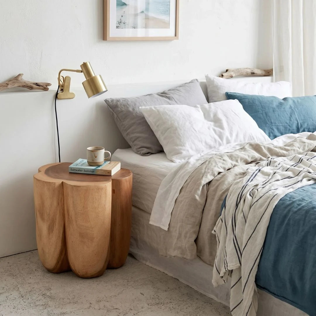 Bedroom with wooden side table, bed with pillows, and lamp.