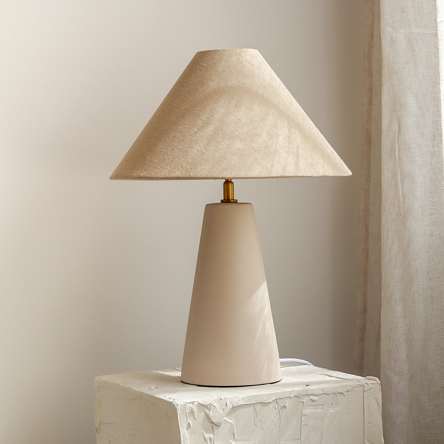 Beige table lamp with a textured shade on a white surface against a beige wall.