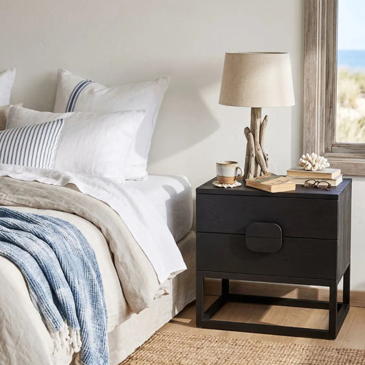 Black nightstand with decorative items next to a bed in a bedroom.