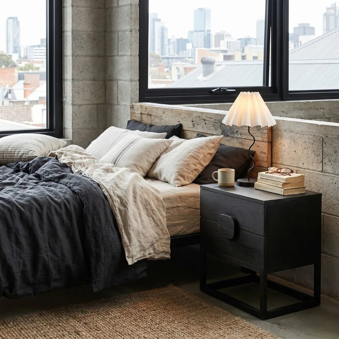 Cozy bedroom with a bed, nightstand, and city view through large windows.