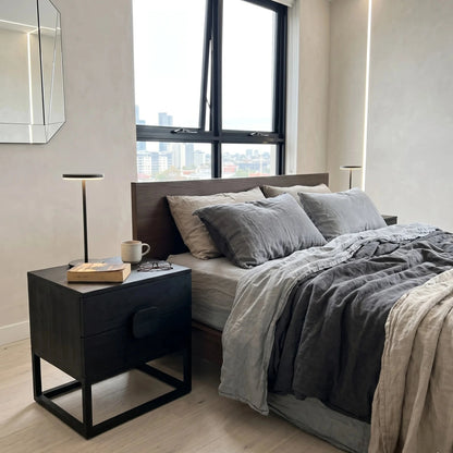 Modern bedroom with a bed and nightstand near a window with cityscape view.