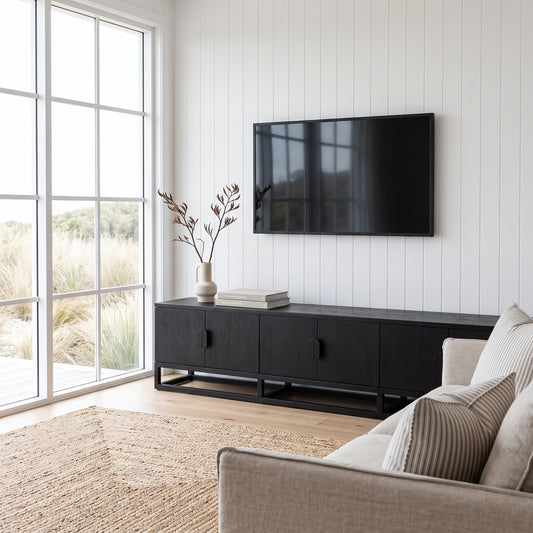 A modern living room scene featuring a black wooden media console with a mounted flat-screen TV on a white shiplap wall, next to a light beige sofa and a large window looking out to grassy land.