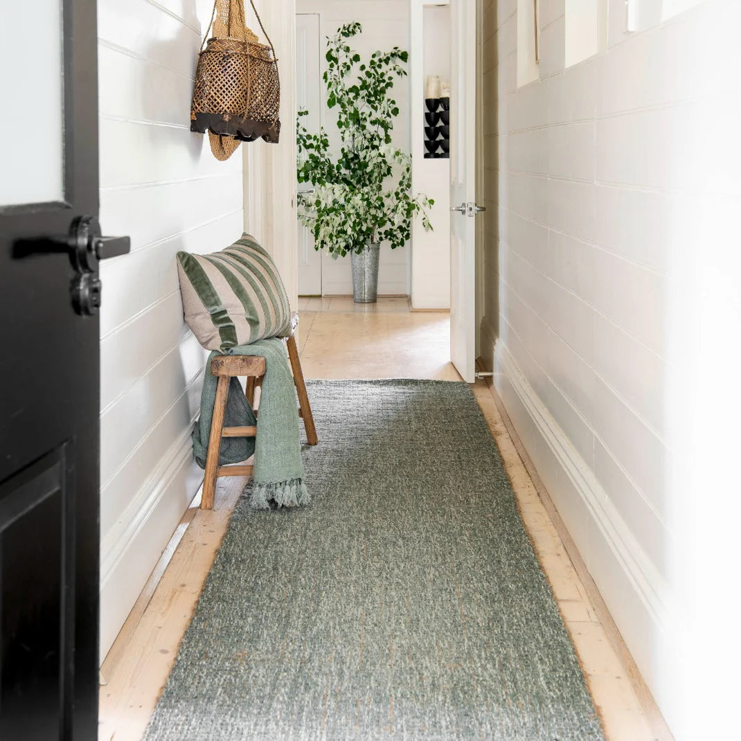 Narrow hallway with a green runner, wooden stool, and decorative items.