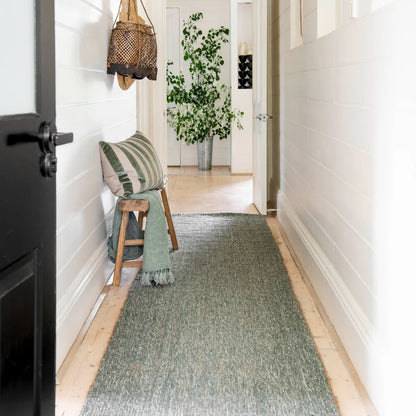 Narrow hallway with a green runner, wooden stool, and decorative items.