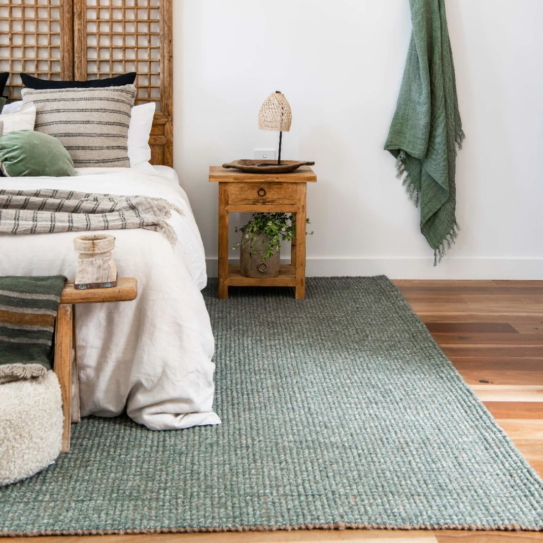 Bedroom with a green rug, wooden nightstand, and white walls.