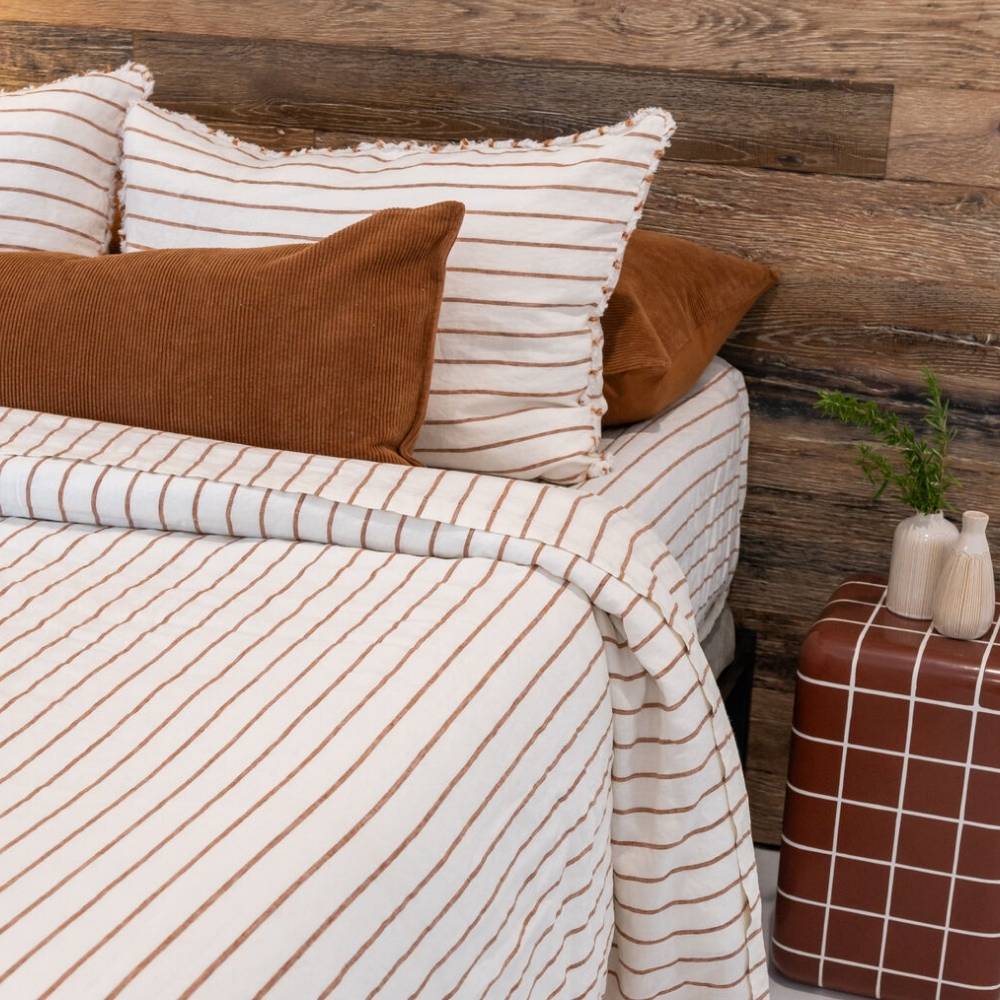 Bed with striped bedding and pillows against a wooden wall.