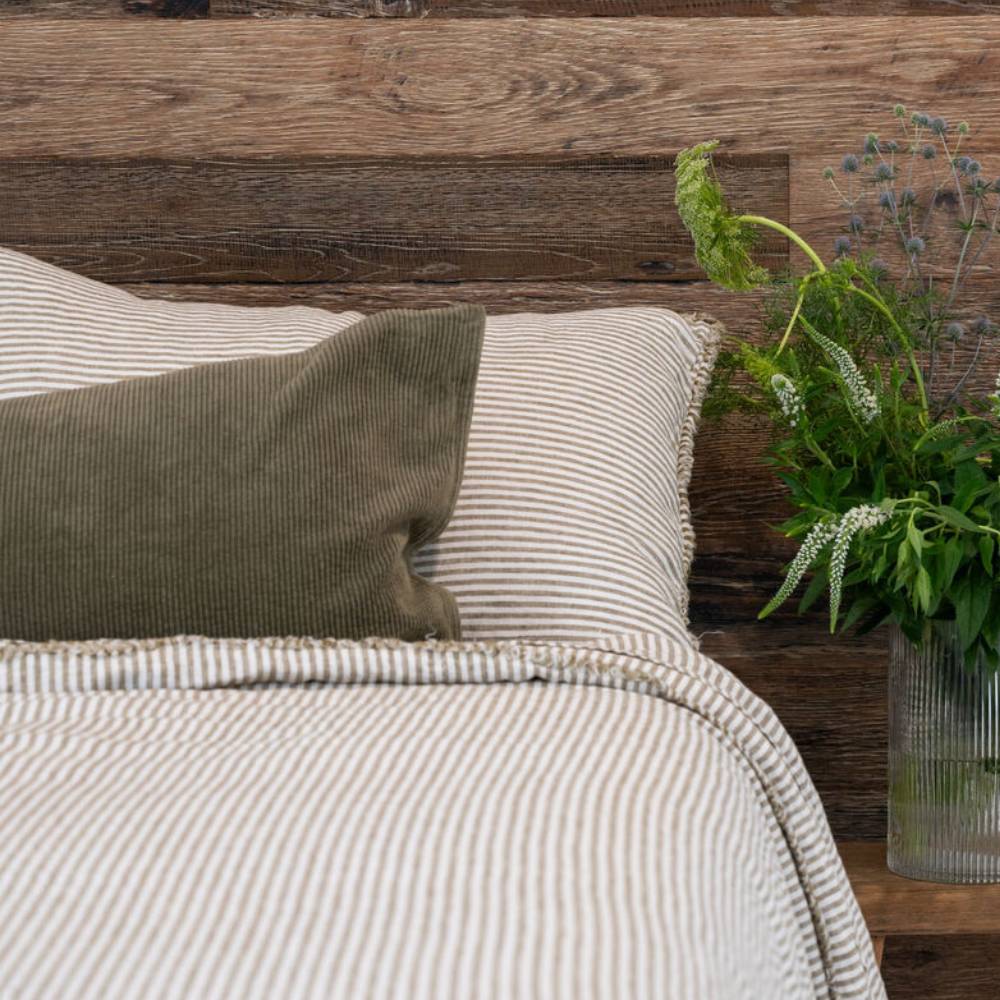 Bed with striped bedding and pillows against a wooden wall with a plant.
