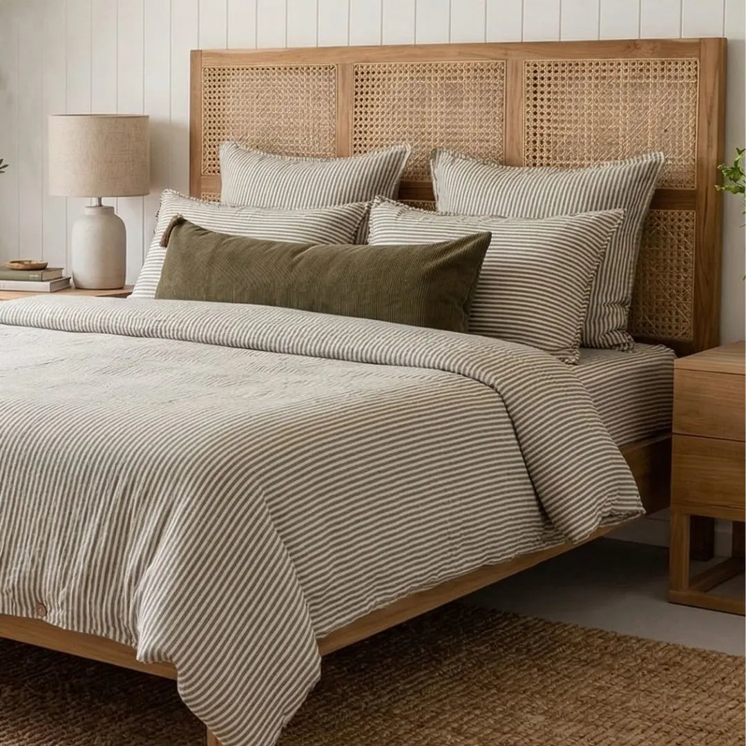 Bedroom with a wooden bed frame, white and olive pin striped french linen bedding, and a lamp.