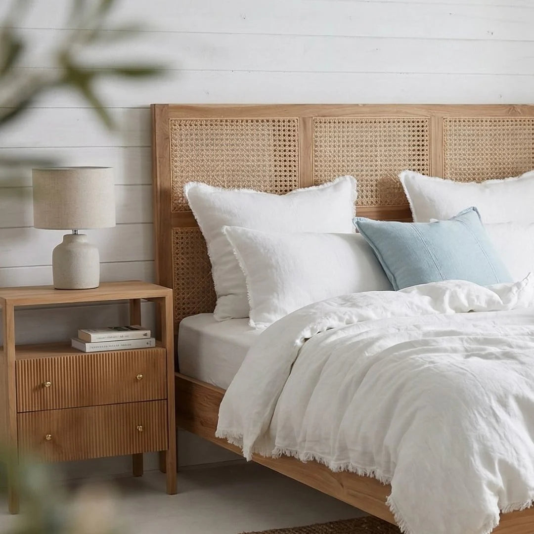 Bedroom with wooden bed and nightstand, featuring white bedding and a lamp.