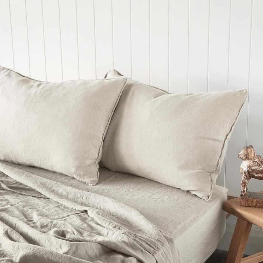 Neatly made bed with beige bedding and pillows against a white paneled wall.
