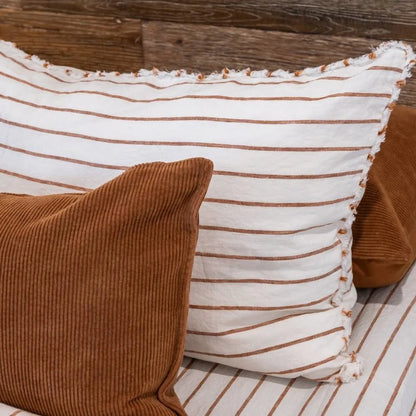 Two brown pillows and a white pillow with brown stripes on a wooden surface.