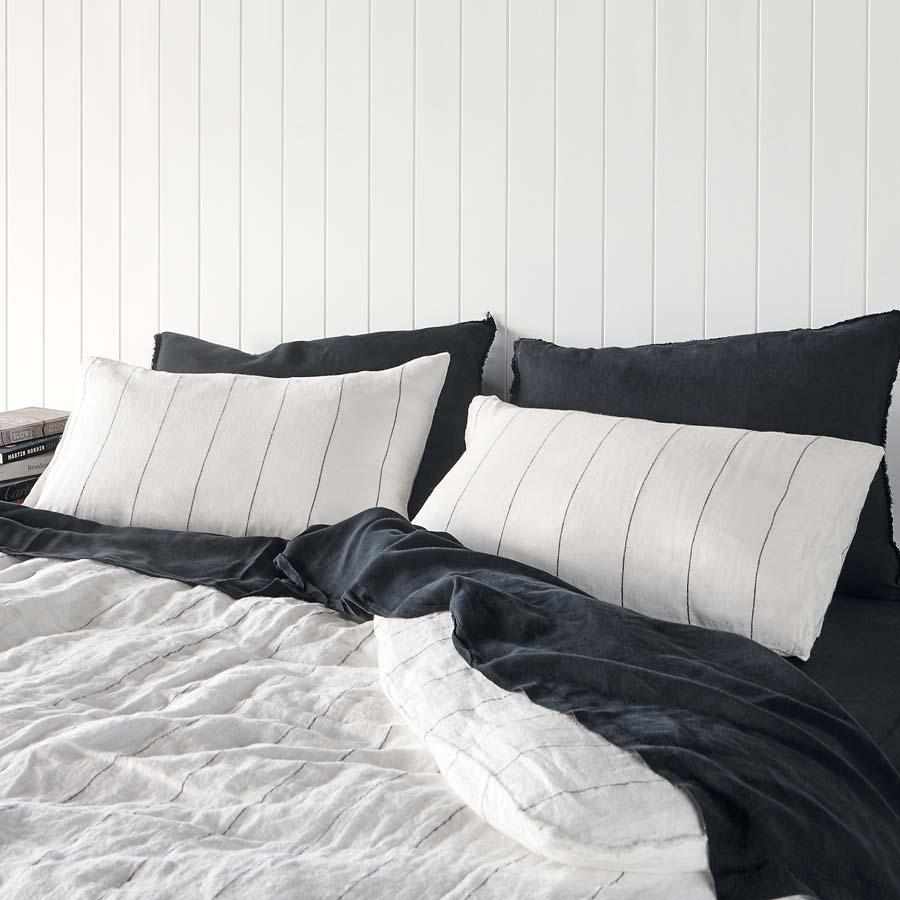 Bed with black and white striped bedding against a white wooden panel wall.