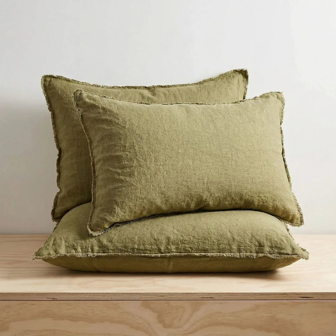 Three olive green pillows on a wooden surface with a neutral background
