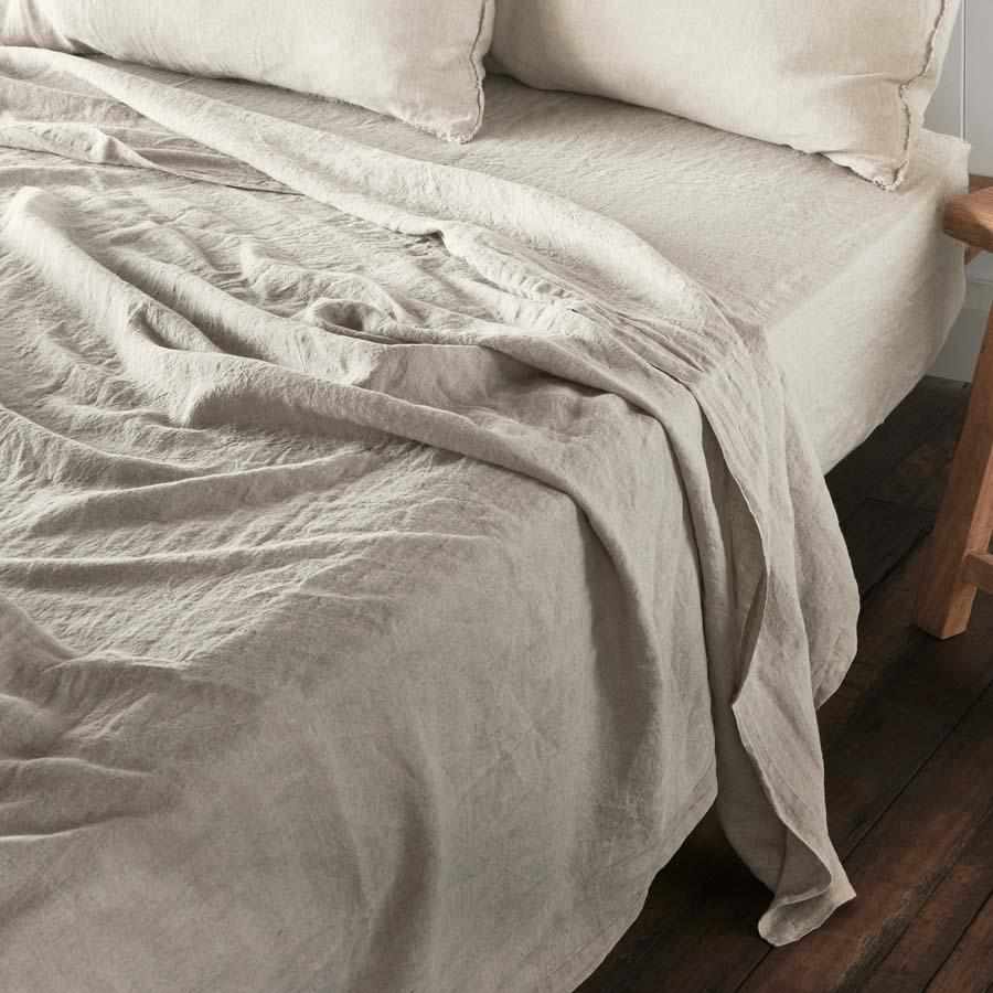 Neatly made bed with light-colored natural french linen bedding on a wooden floor.
