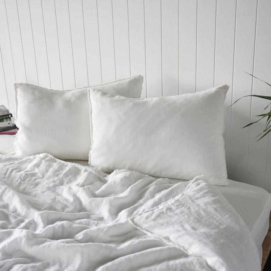 White french linen bedding set with two pillows on a bed against a white paneled wall.