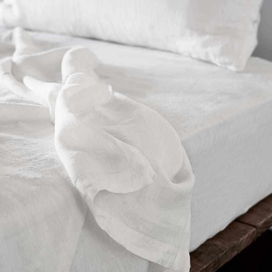 White french linen sheets draped over a bed with pillows