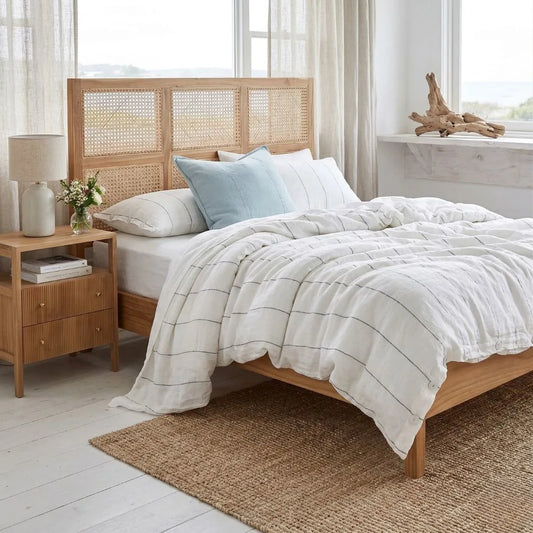 Bedroom with wooden bed, wicker headboard, nightstand with lamp with Sun Republic French Linen Duvet cover and pillows