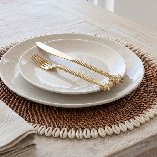 White ceramic plate with gold cutlery on a woven placemat