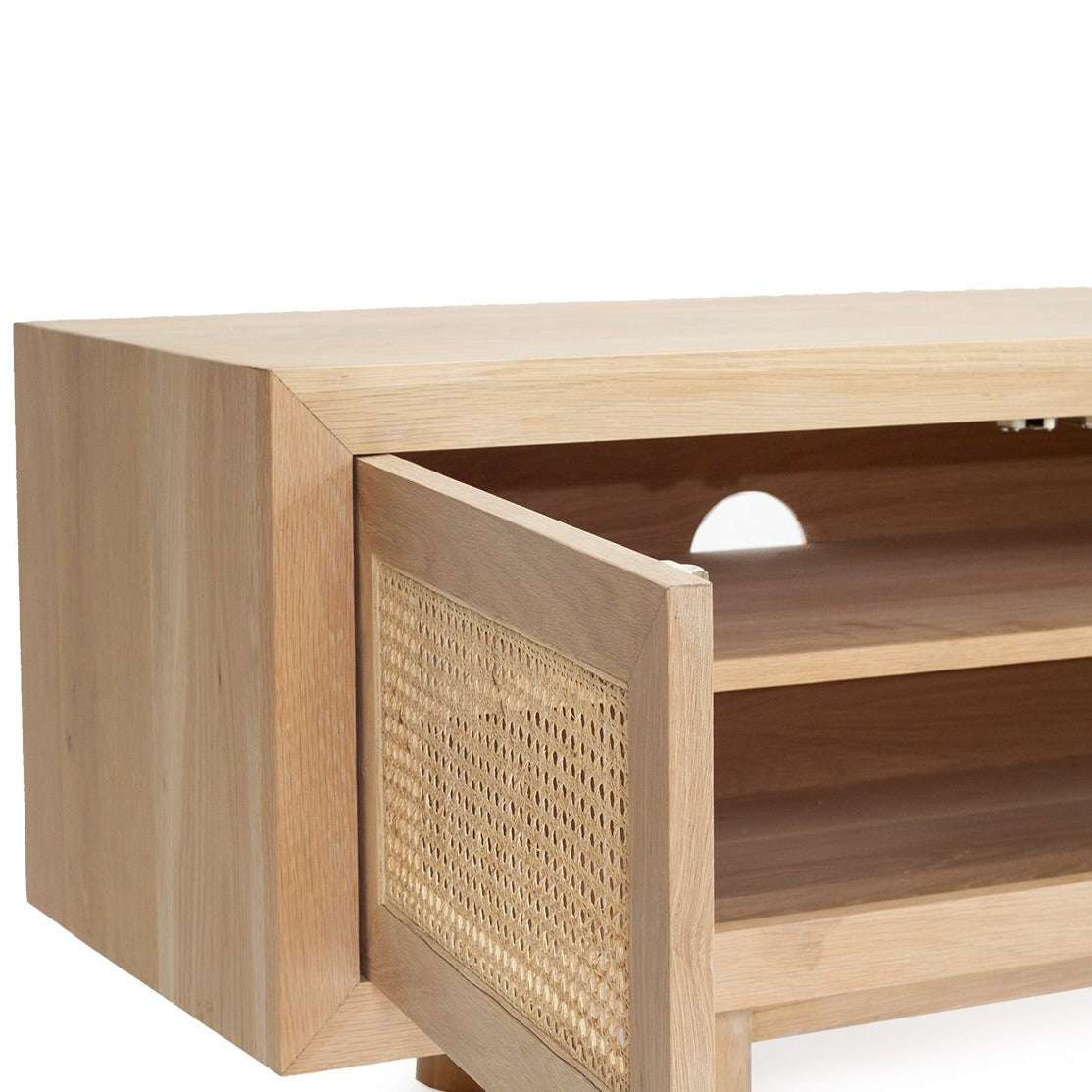A close-up of a light natural wood media console or cabinet with an open door featuring woven cane panels, showing the interior shelves against a white background.