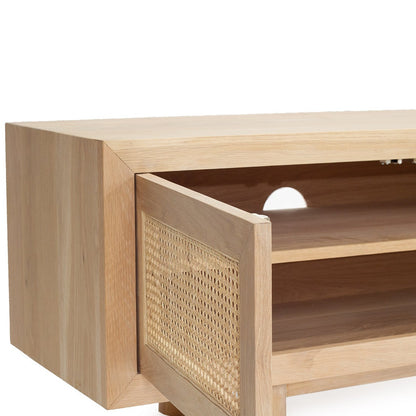 A close-up of a light natural wood media console or cabinet with an open door featuring woven cane panels, showing the interior shelves against a white background.