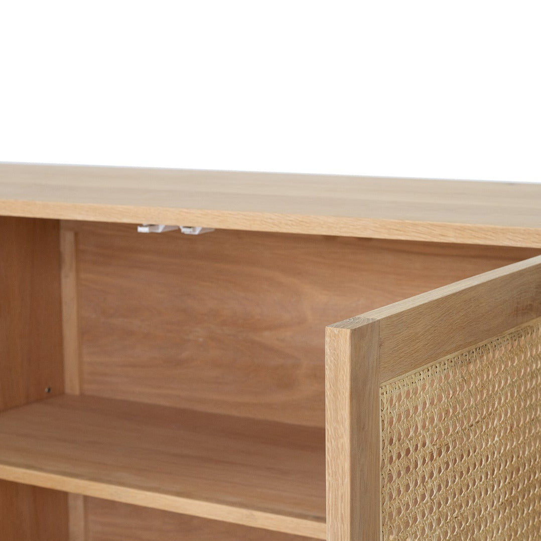 Close-up of a light natural wood cabinet or shelf unit with an open door showing a woven cane panel on the right side and a wooden shelf inside.