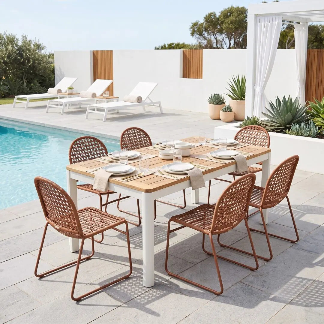 Outdoor dining set with a rectangular wooden table and six woven rattan chairs in a modern patio setting next to a swimming pool.