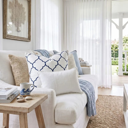 Cozy living room with a white sofa adorned with patterned cushions, a wooden coffee table, and a view of a garden.