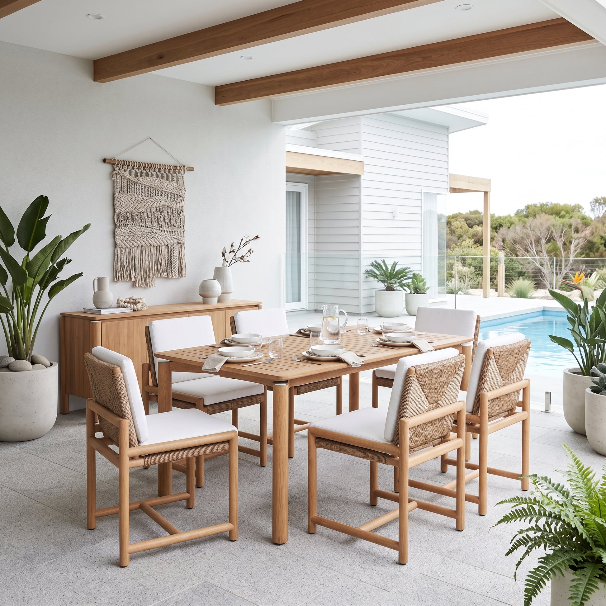 A modern dining set consisting of a rectangular light oak table and six matching chairs with white cushions and woven cane backs, styled on a tiled patio next to a swimming pool.