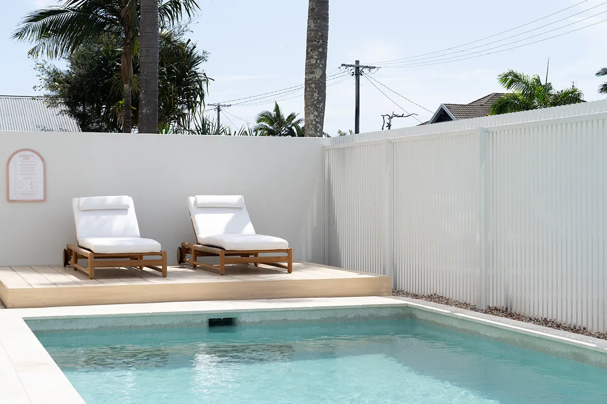 Two white lounge chairs by a pool with palm trees in the background