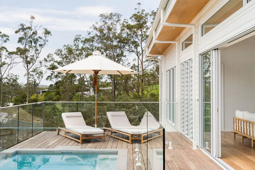 Modern poolside deck with lounge chairs, umbrella, and glass walls.