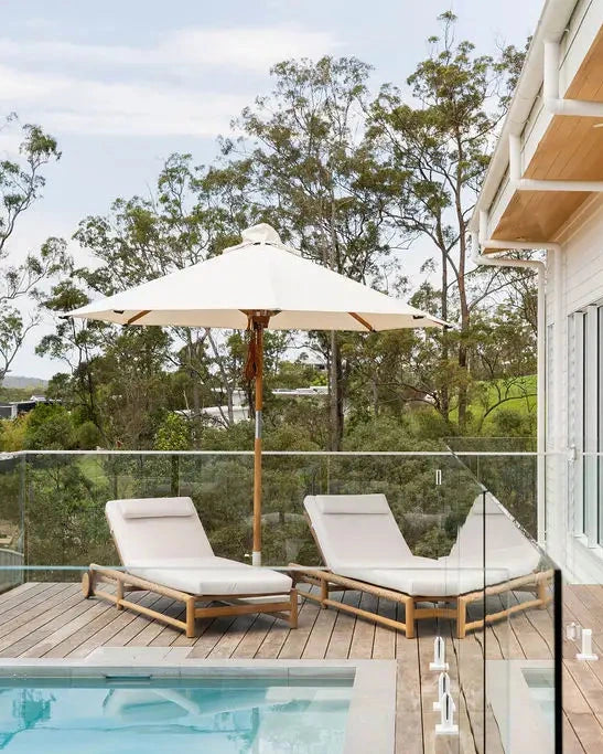 Modern poolside deck with lounge chairs, umbrella, and glass walls.