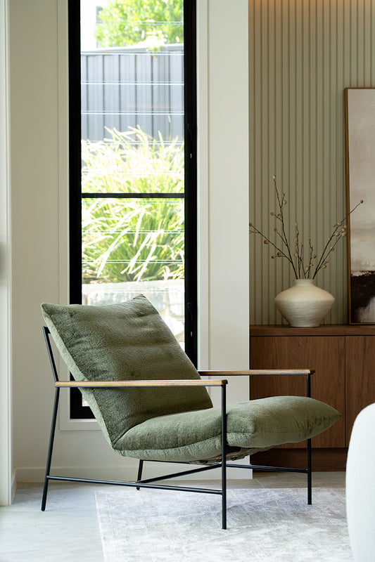 Green armchair in a modern living room with a large window and decorative elements.