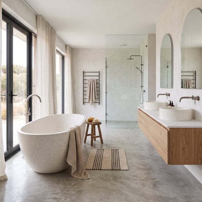A modern bathroom interior with a freestanding oval stone bathtub, double vessel sinks on a floating wood vanity, a glass shower enclosure, large arched mirrors, and floor-to-ceiling windows with sheer curtains.