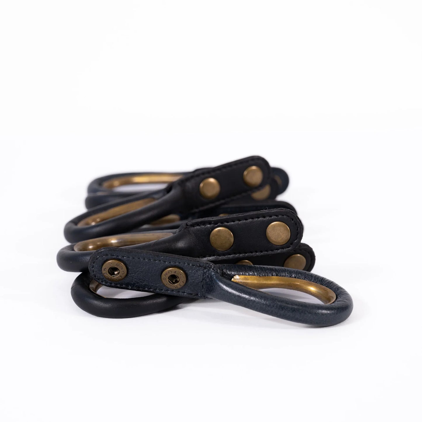 Set of black leather curtain rings with brass hardware on a white background