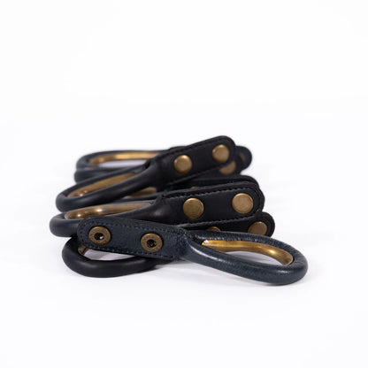 Set of black leather curtain rings with brass hardware on a white background