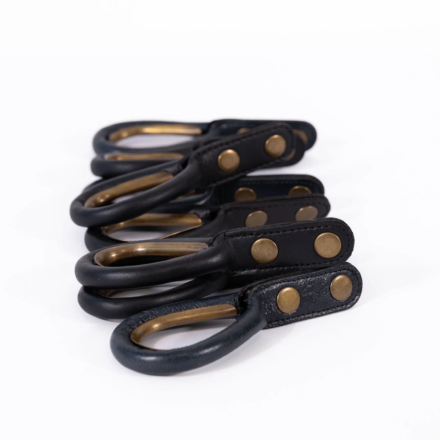 Set of black leather curtain rings with brass hardware on a white background