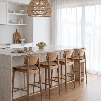 Four wooden bar stools with light wood frames and woven seats, arranged around a white marble kitchen island in a bright, modern kitchen.