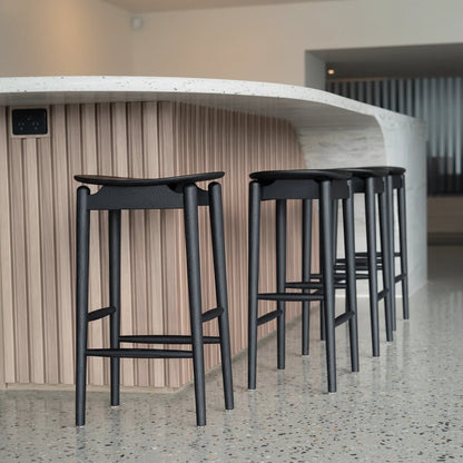 Row of black bar stools against a wooden paneled wall.
