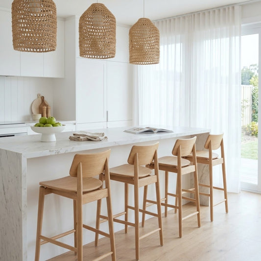 A bright modern kitchen with a white marble island, four light wood bar stools, and three woven wicker pendant lights hanging above.