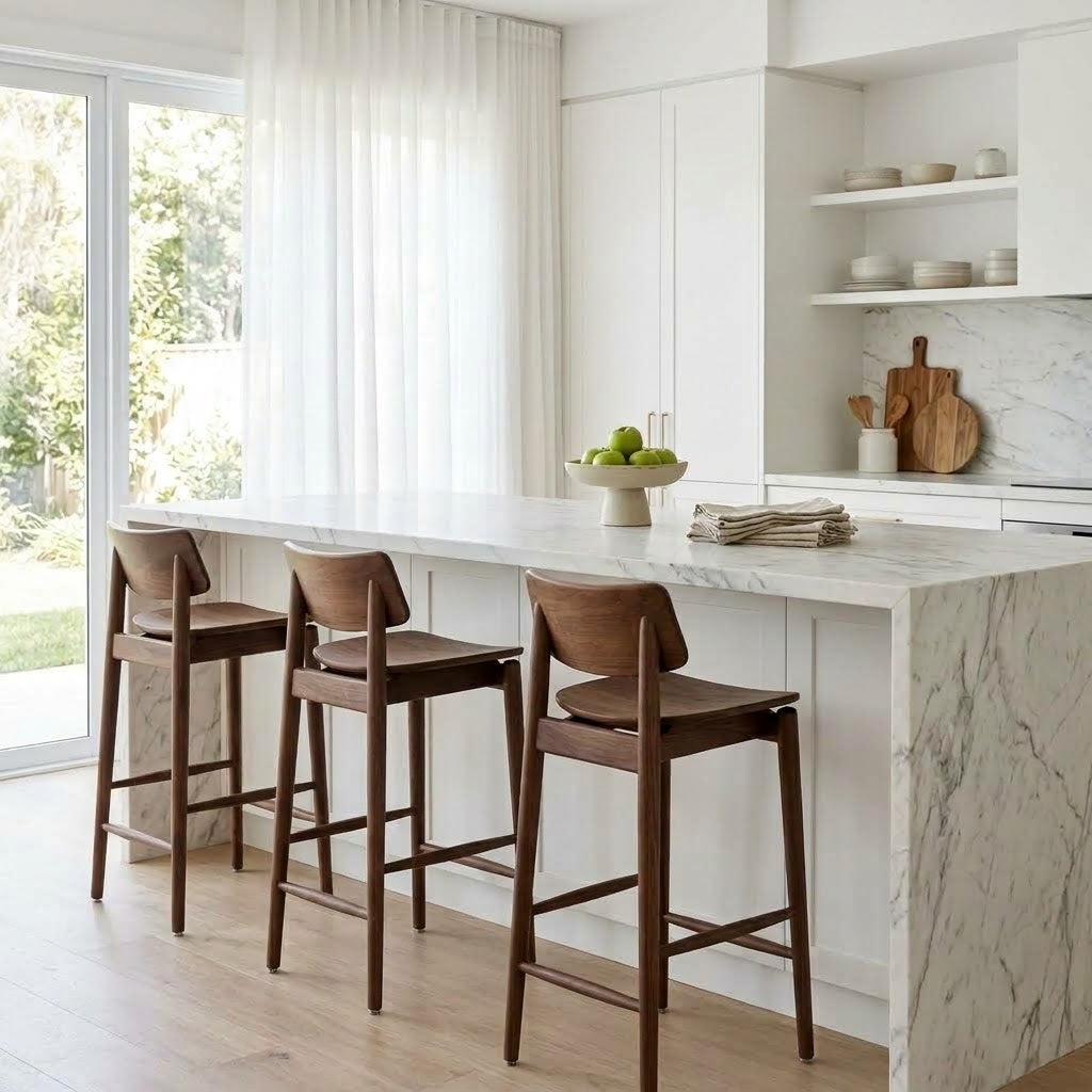 Three wooden bar stools with dark brown wood frames and light beige seats, arranged along a white marble kitchen island in a bright, modern kitchen.