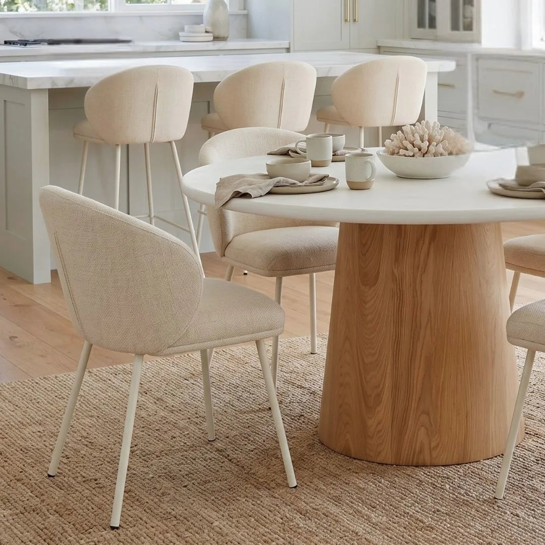 Close up of a the round microcement dining table with natural oak base, linen dining chairs in an modern coastal open plan kitchen dining home by sun republic