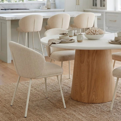 Close up of a the round microcement dining table with natural oak base, linen dining chairs in an modern coastal open plan kitchen dining home by sun republic